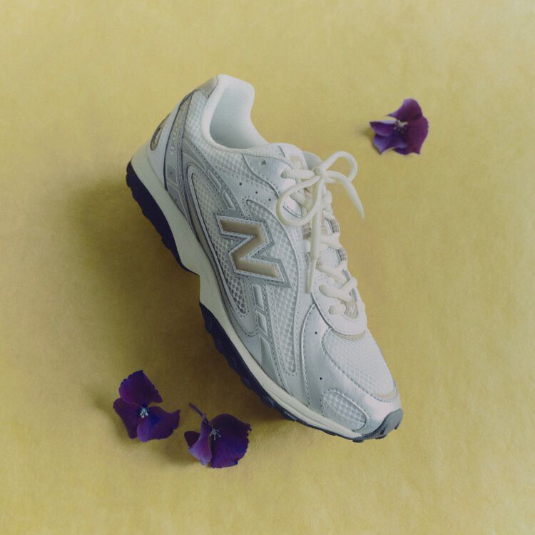 A grey shoe laying sideways with purple flowers surrounding it. 