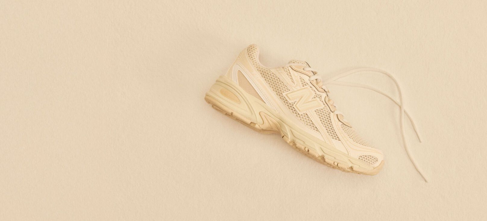 A tan shoe laying on a tan studio backdrop. 