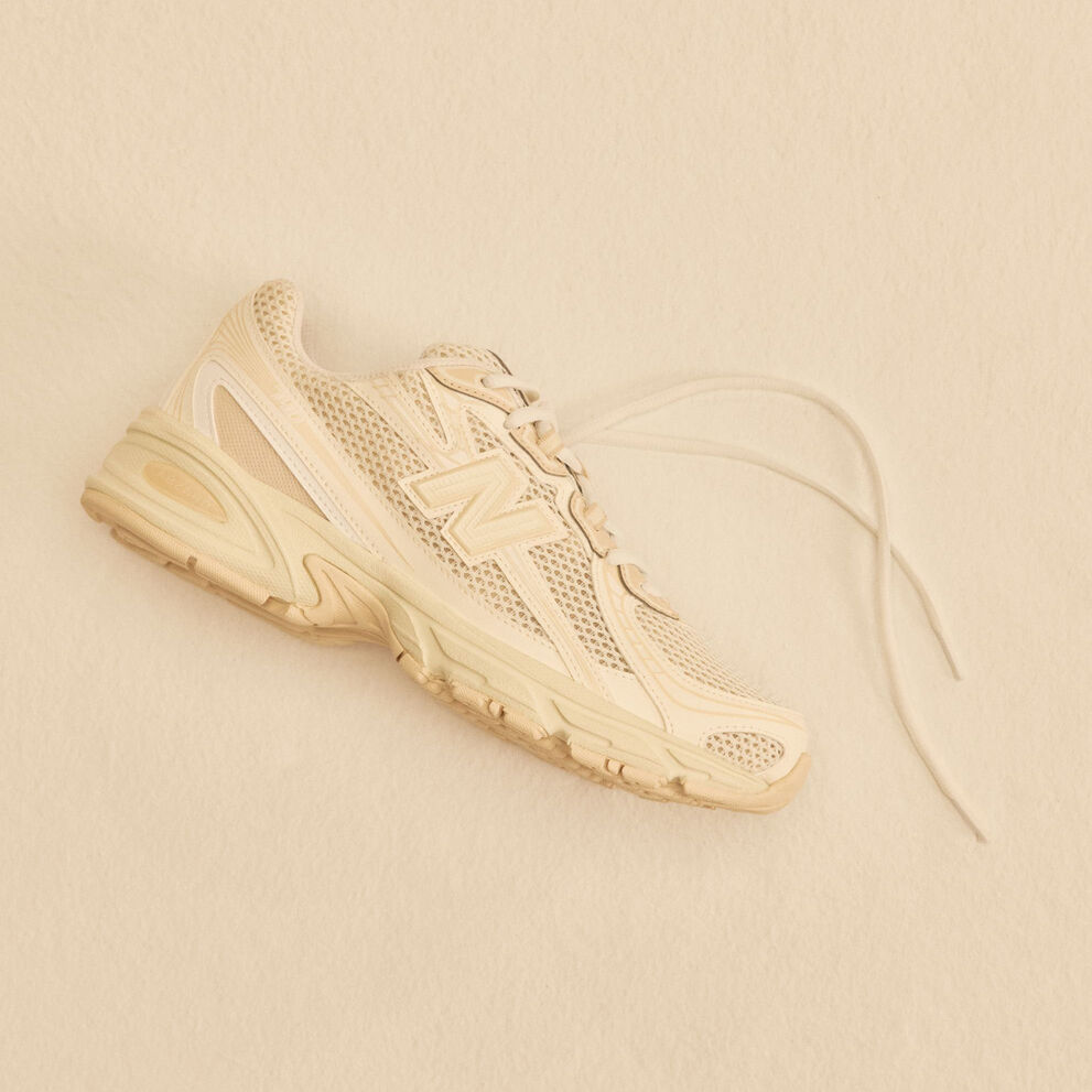 A tan shoe laying on a tan studio backdrop. 
