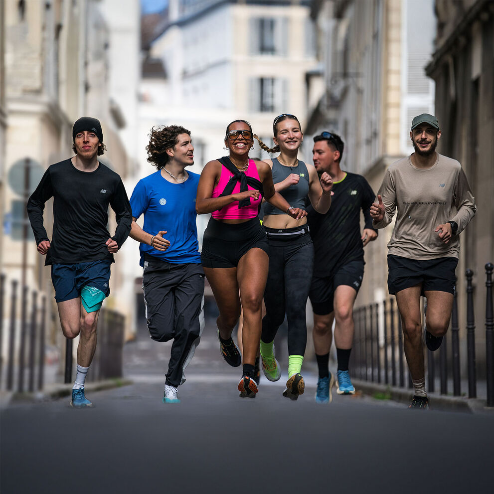 A smiling and happy group of runners in New Balance running apparel, running together through a charming Parisian neighborhood with historic buildings and picturesque streets in the background.