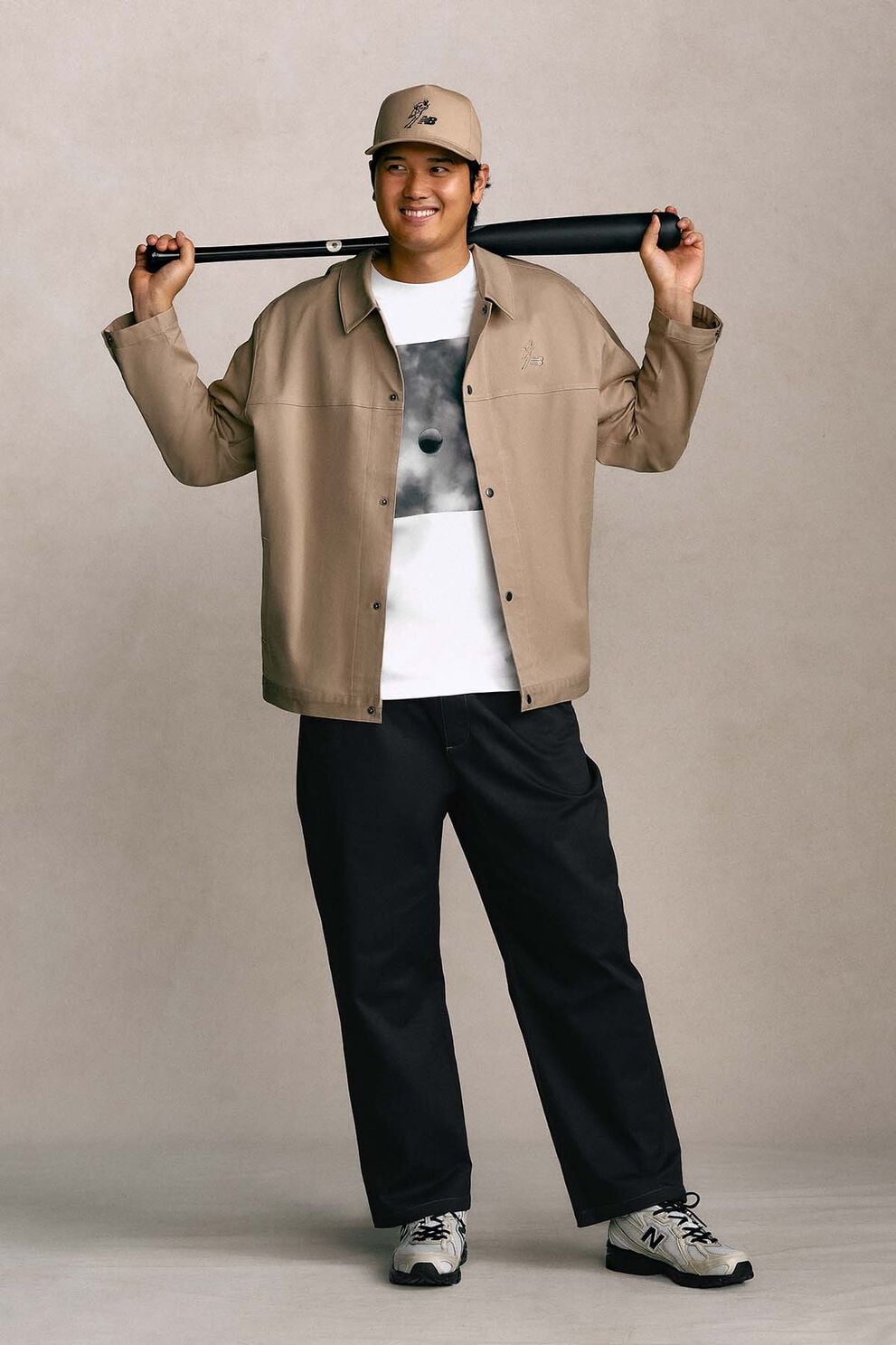 Shohei Ohtani standing against a tan studio backdrop holding a baseball bat.