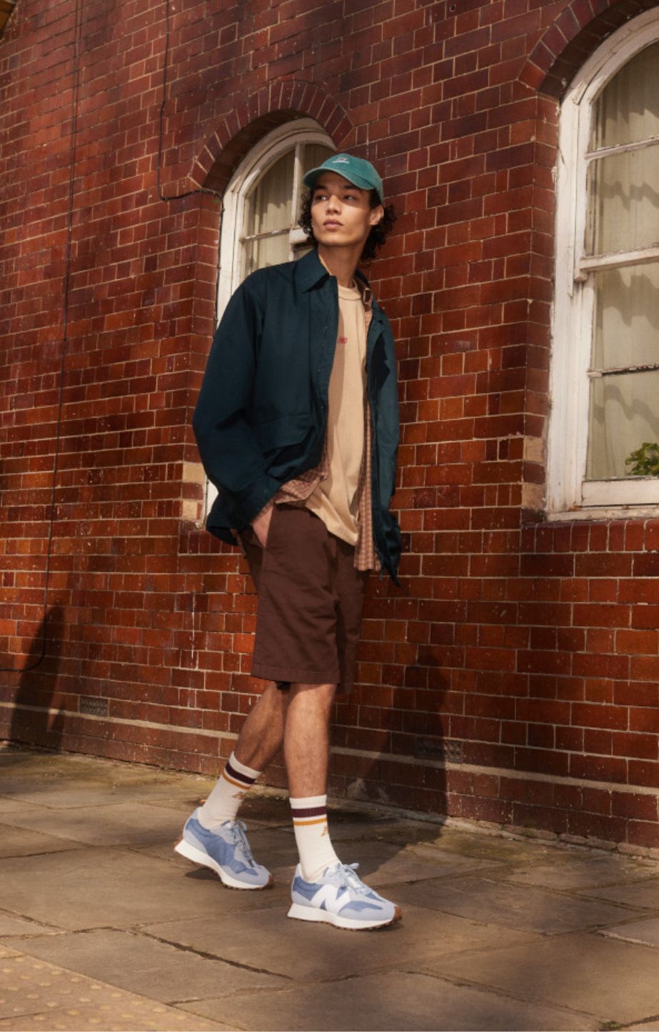 A man waking in the street in front of a brick wall wearing New Balance 327 shoes and apparel