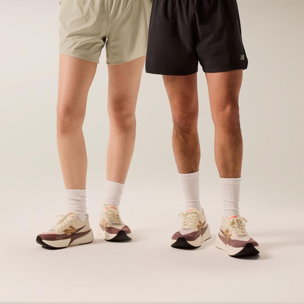 Young couple standing in front of a beige background in white and black shorts with brown running shoes. 
