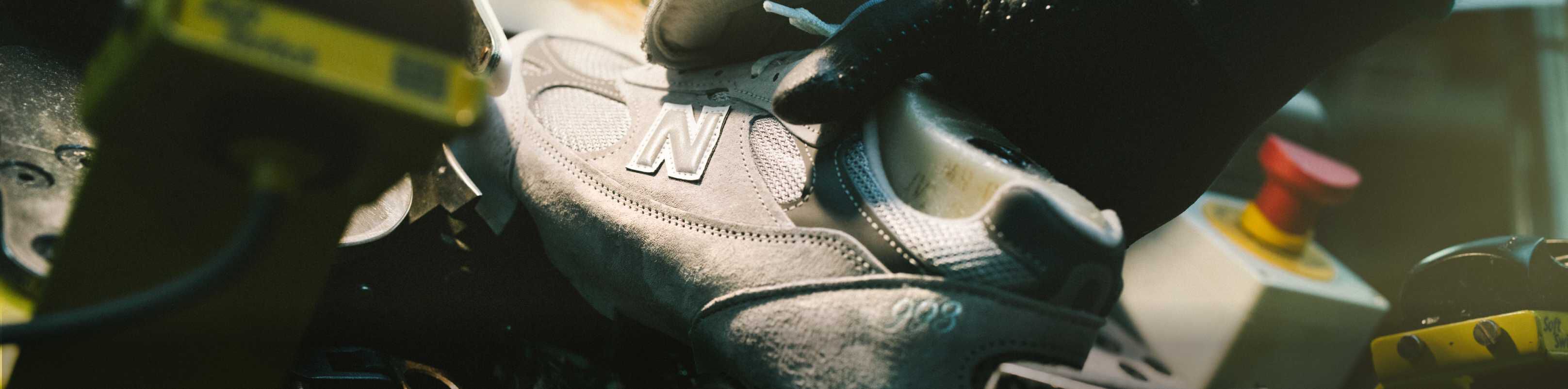 A New Balance sneaker sitting in equipment and being constructed in a factory setting. 