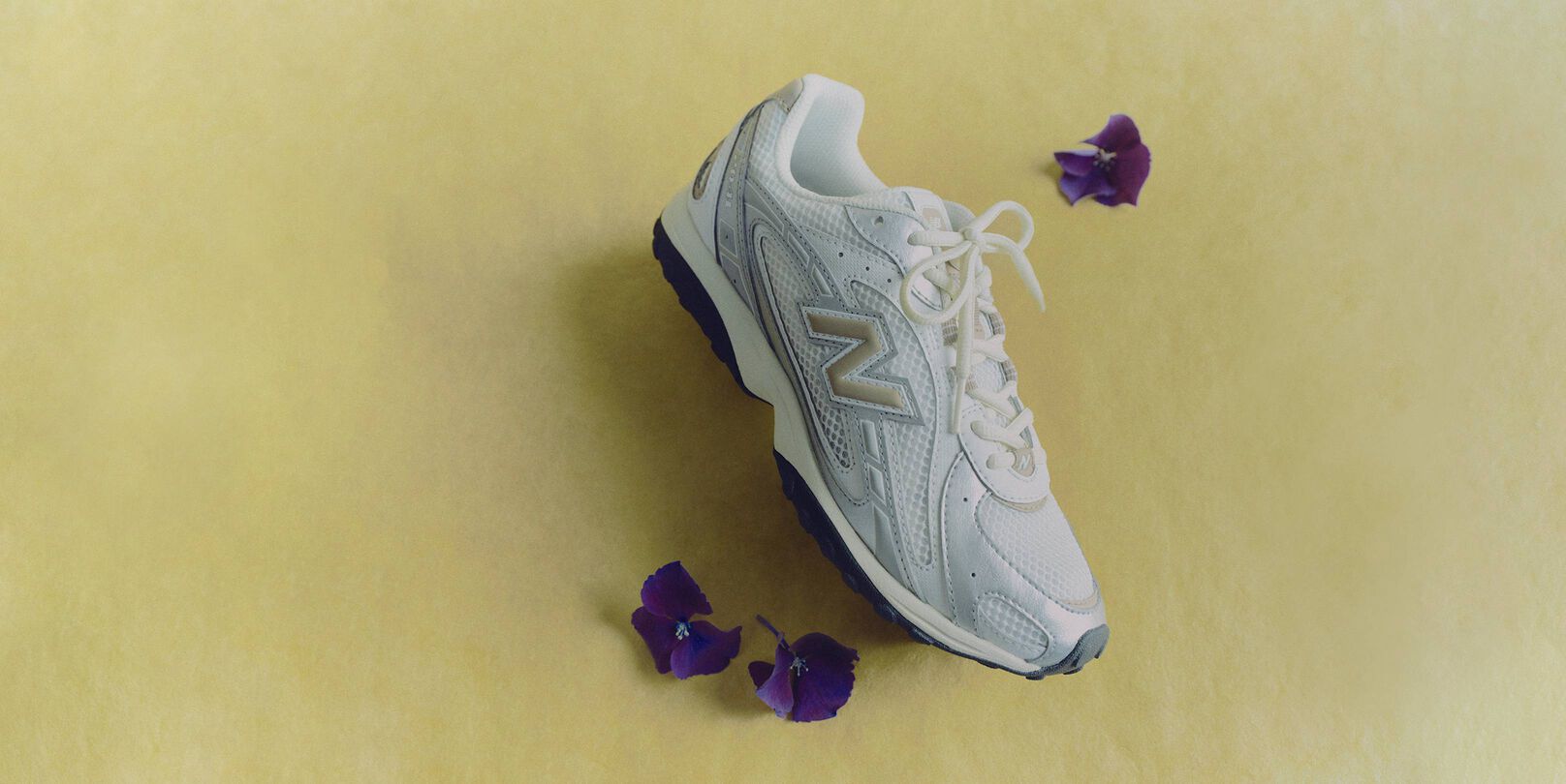A grey shoe laying sideways with purple flowers surrounding it. 