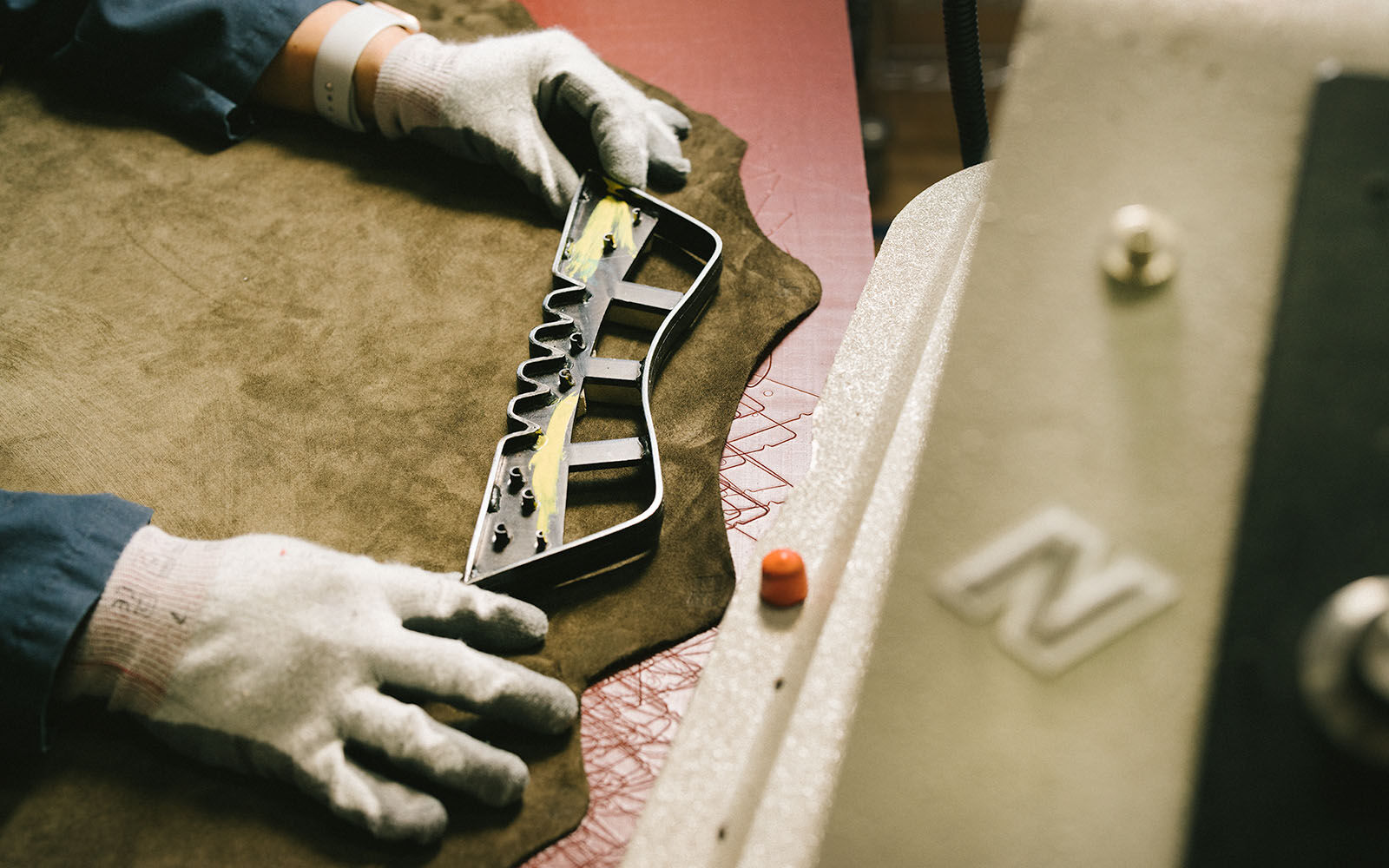A pair of hands laying a tool over a piece of suede in a factory setting.