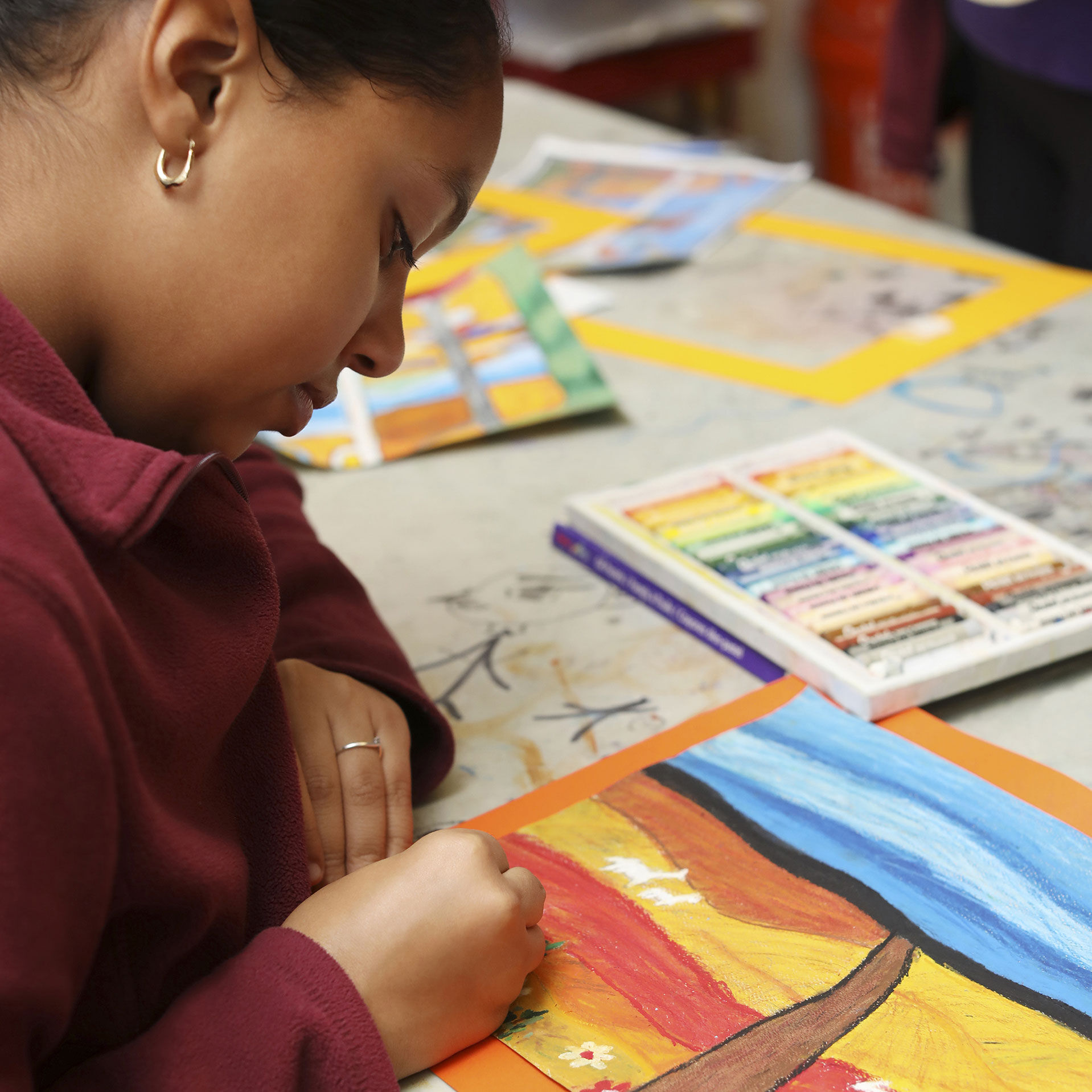 A medium-skinned, female-presenting teen working intently on a drawing of a landscape.
