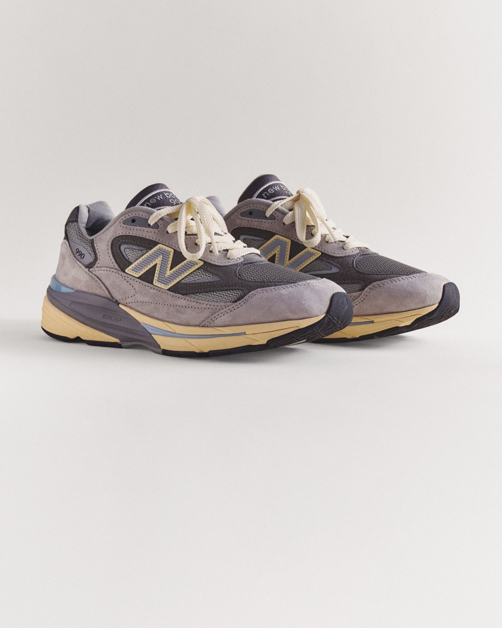 A pair of grey 990v7 sneakers sitting on a grey studio backdrop.